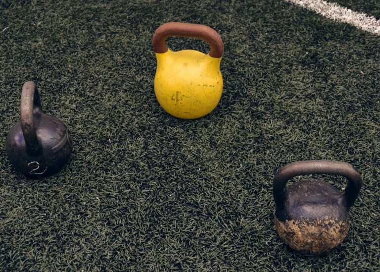 Drei Kettlebells liegen auf einer Rasenfläche im Freien