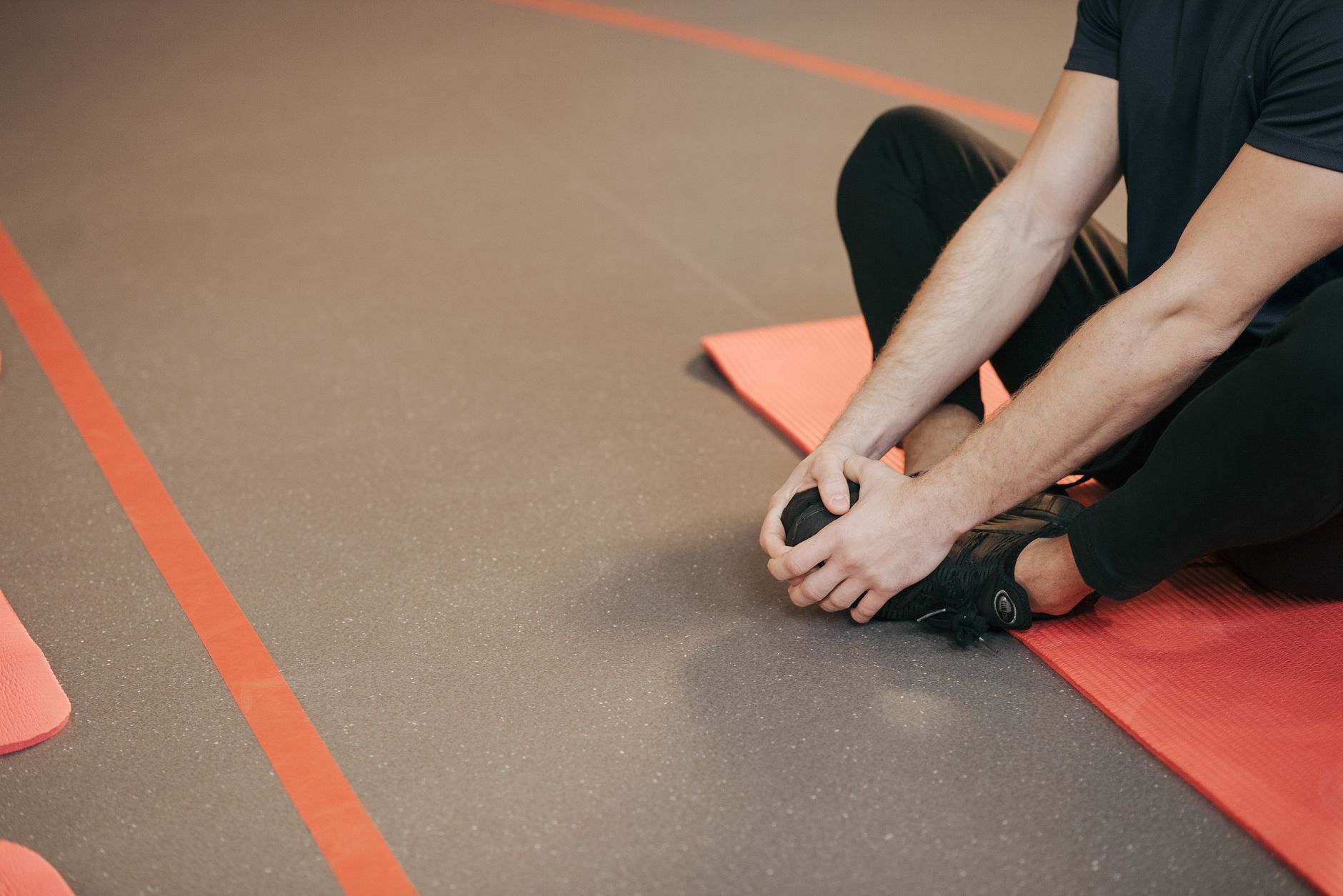 Mann dehnt im Sitzen den Fuß auf einer Gymnastikmatte