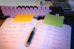 Notizbuch mit abgehakter Checkliste und Haftnotizen neben einer Tastatur