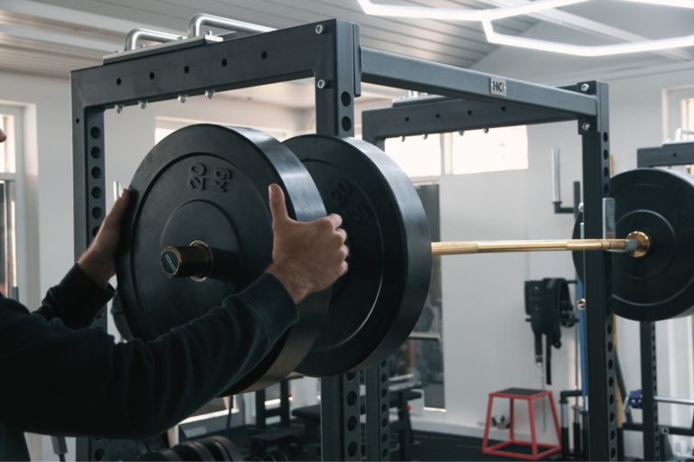 Hände schieben eine Gewichtsscheibe auf eine Langhantel im Squat-Rack