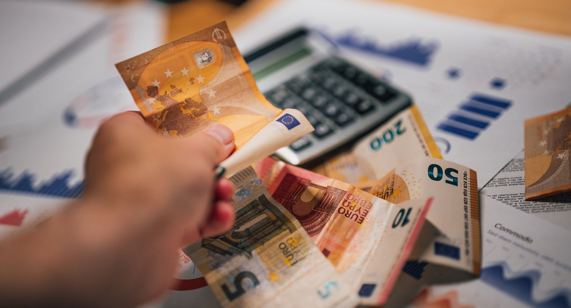 Hand mit Euro-Scheinen über Auswertungen und einem Taschenrechner