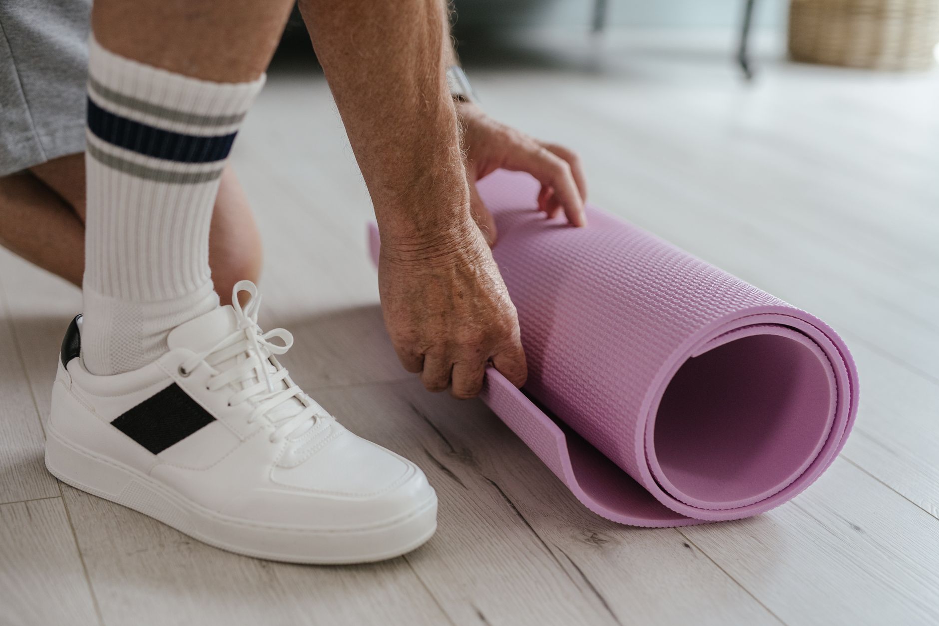 Person rollt zu Hause eine Gymnastikmatte auf dem Holzboden aus
