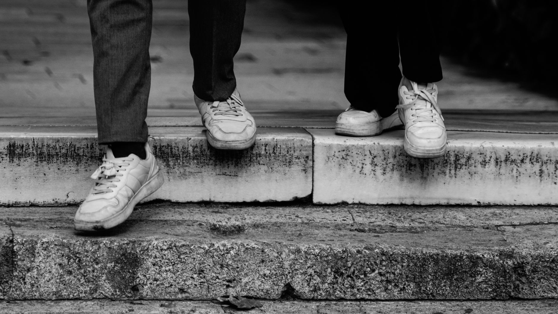 Beine zweier Personen in Turnschuhen beim Hinabsteigen einer Steintreppe, Schwarz-Weiß-Aufnahme